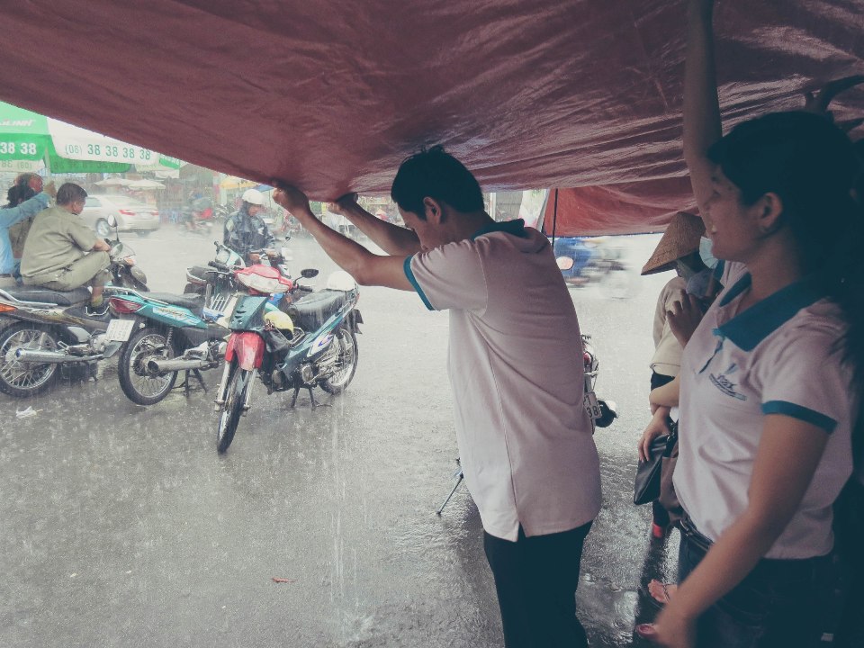 Cơn mưa vẫn kéo dài các thành viên VTAX giữ mái che để bảo về những hộp cháo